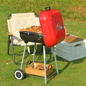 Parrilla con Tapa roja en el jardín con carne asándose sobre el césped.